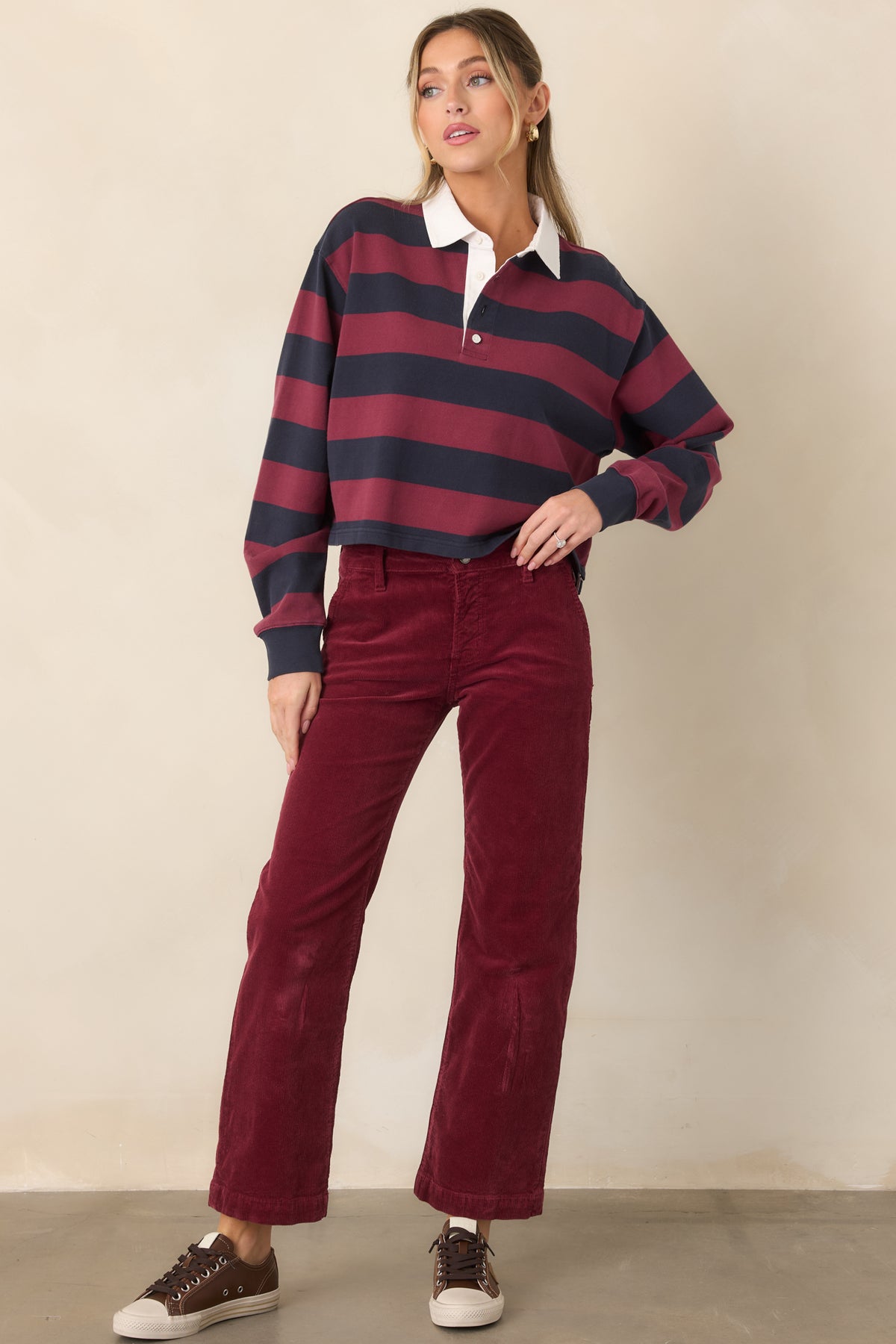 Wide-striped cropped polo top with relaxed shoulders, long sleeves, contrasting white collar, sporty partial button closure, and a straight hem.