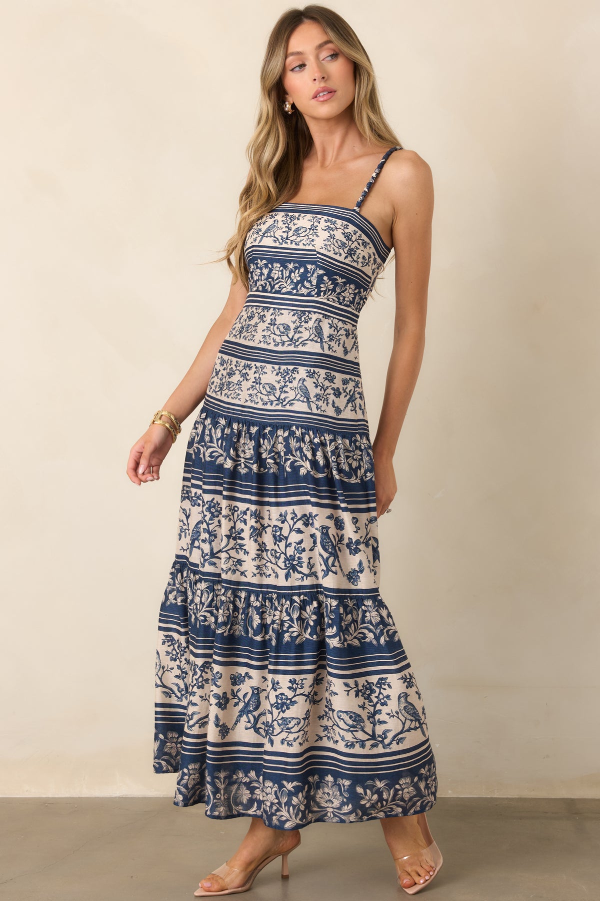 Winding branches, perched birds, and floral borders create a detailed pattern throughout the elongated bodice and voluminous skirt.