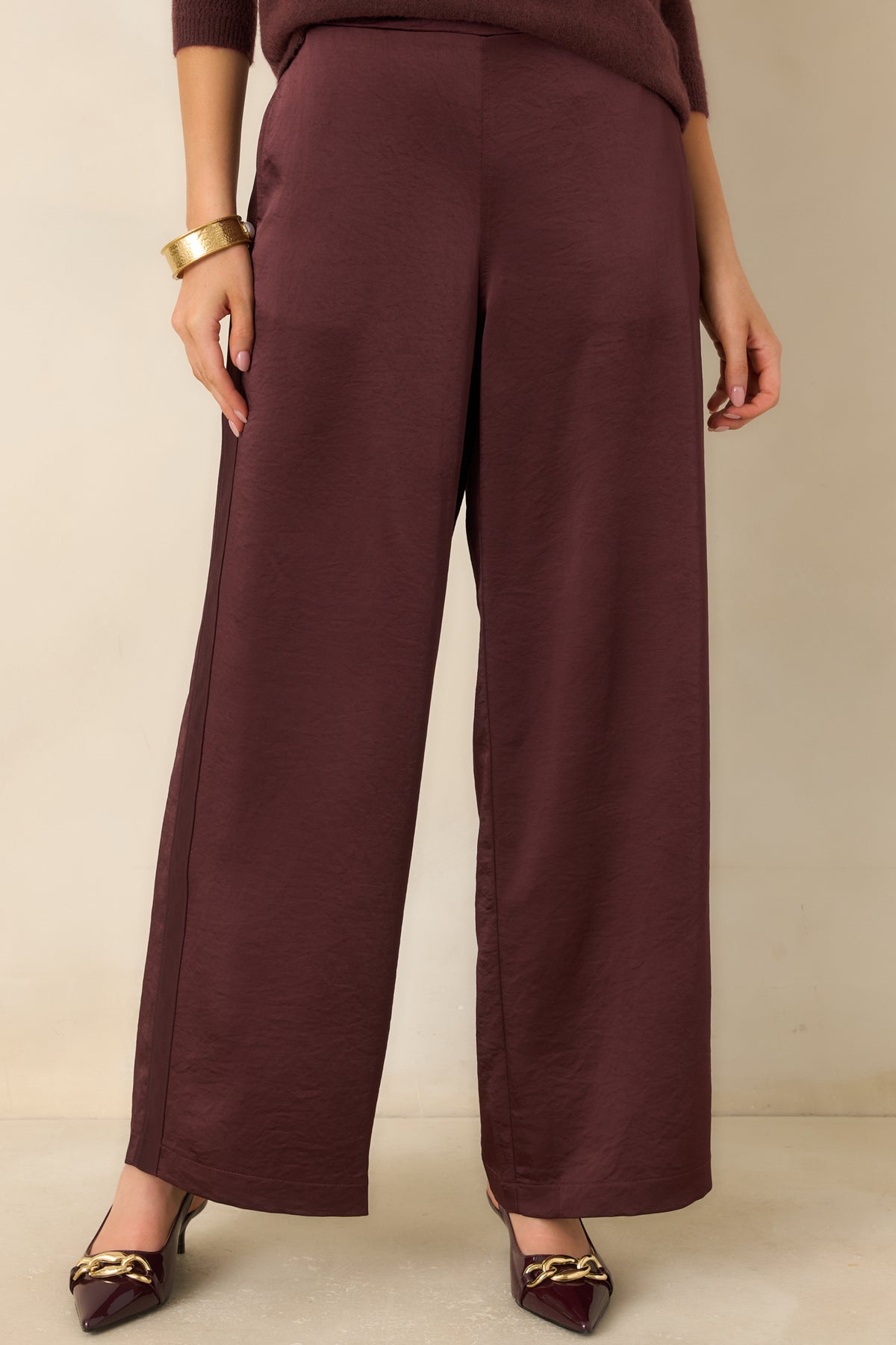 Subtle sheen and soft texture highlight the rich wine color across the pants’ wide-leg fabric.