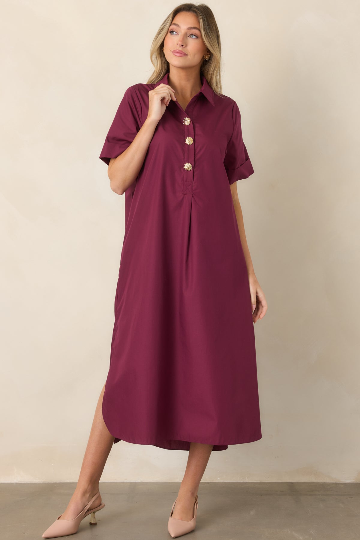 Wine red shirt-style maxi dress showcasing its relaxed A-line silhouette, collared neckline, rolled short sleeves, and decorative gold floral buttons along the front.
