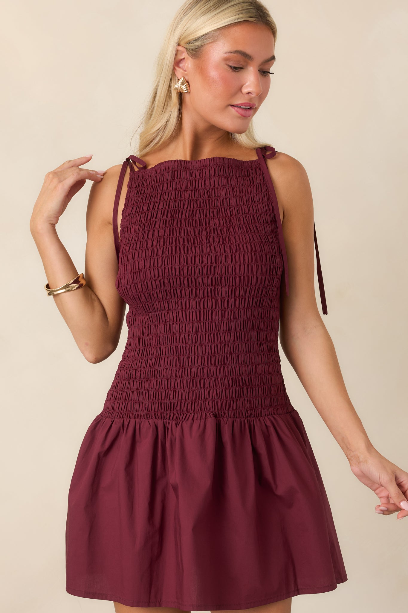 Close view of the wine red mini dress showcasing the fully shirred bodice, high neckline, and adjustable tie straps.