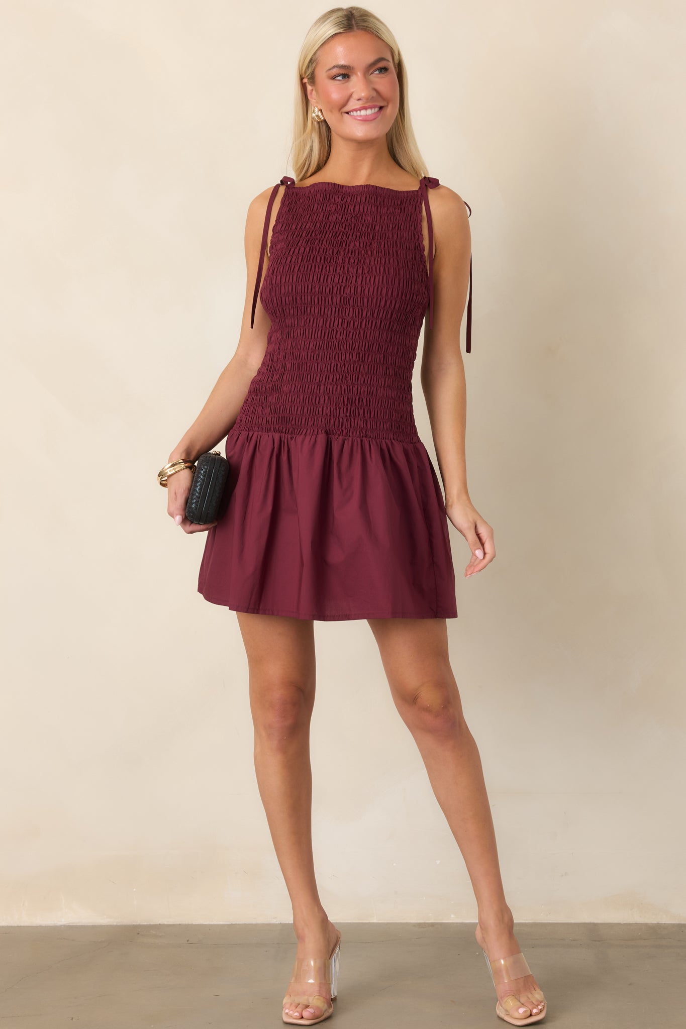 Wine red cotton mini dress featuring a fully shirred bodice, high neckline, adjustable tie straps, softly gathered skirt, and easy flared hem.
