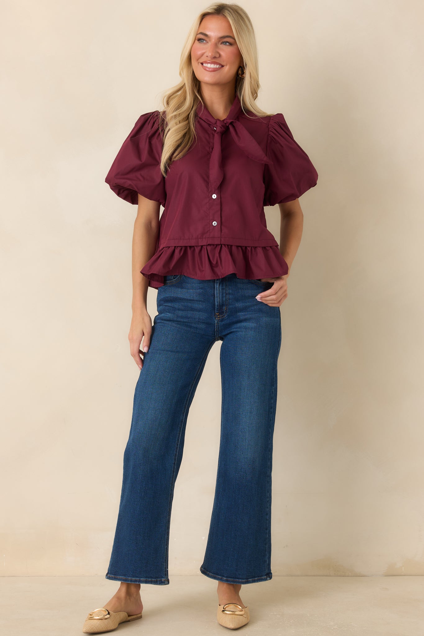 Wine red top featuring a statement bow tie neckline, voluminous puff sleeves, and a feminine flounced peplum hem.