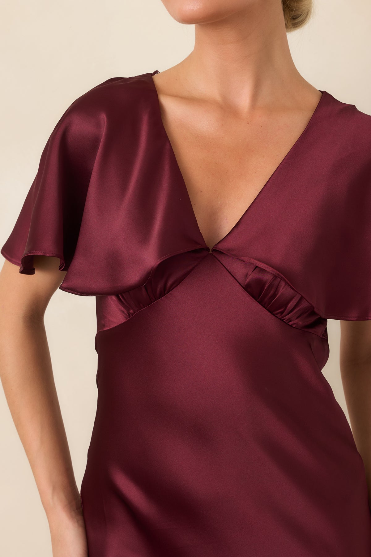 Close-up detail of the wine satin dress showing the plunging V-neckline and defined waist seam.