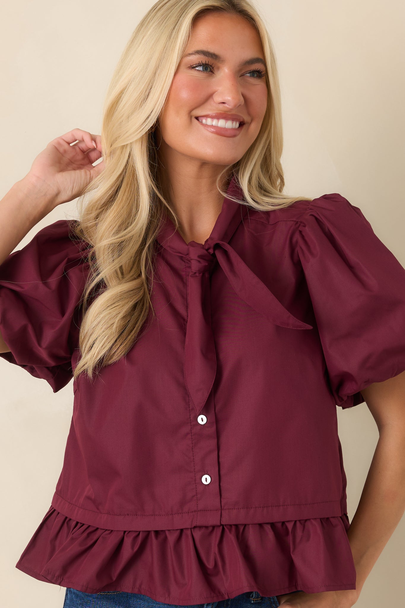 Close view of the wine red top highlighting the oversized bow tie neckline and gathered puff sleeve details.