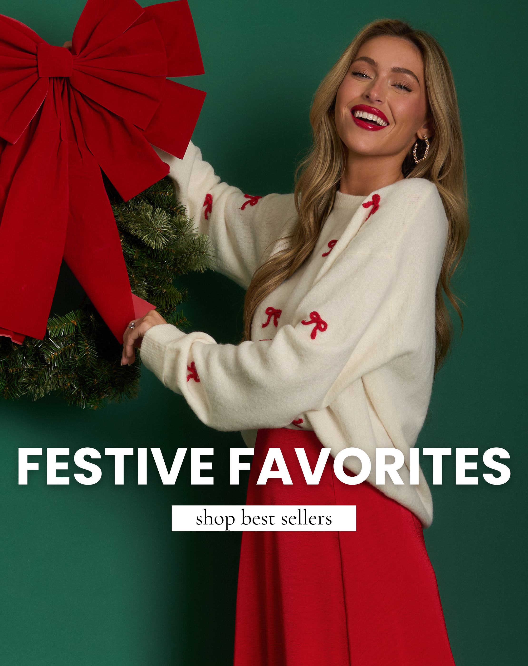 Smiling model in a cream sweater with red bow details and red skirt holds a wreath with a large red bow. Shop festive women’s holiday best sellers.