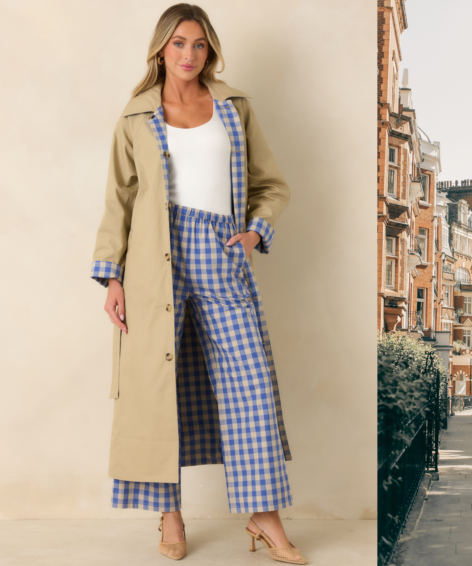 Woman in a reversible neutral trench coat with blue and white gingham lining against a beige background with a scenic London backdrop peeking into the frame. 