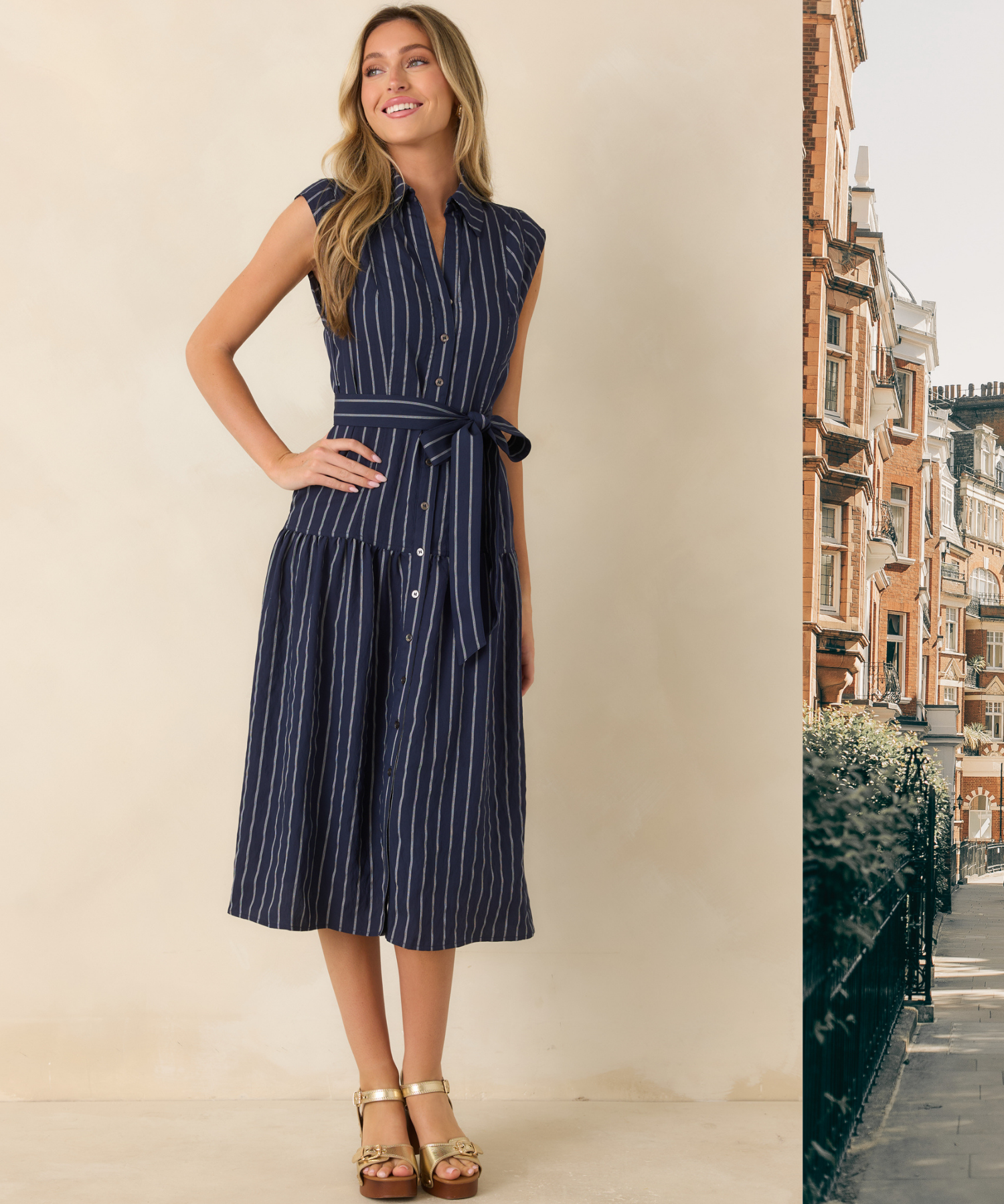 Woman wearing a navy blue stripe midi dress against a beige background, with a scenic London backdrop peeking into the frame. 