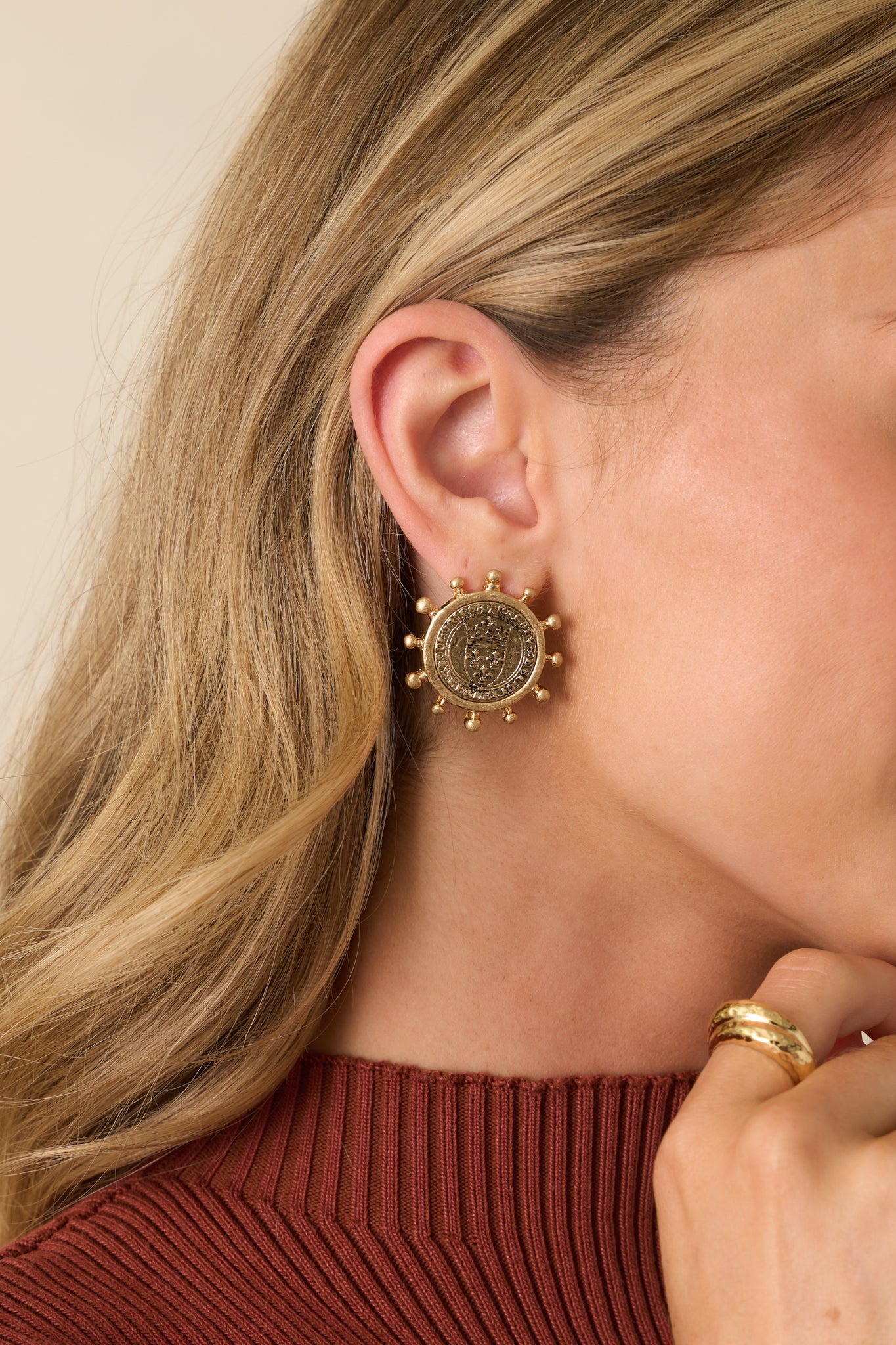 Worn gold earrings with embossed coin medallions framed by tiny ball prongs, shining in a rounded design.