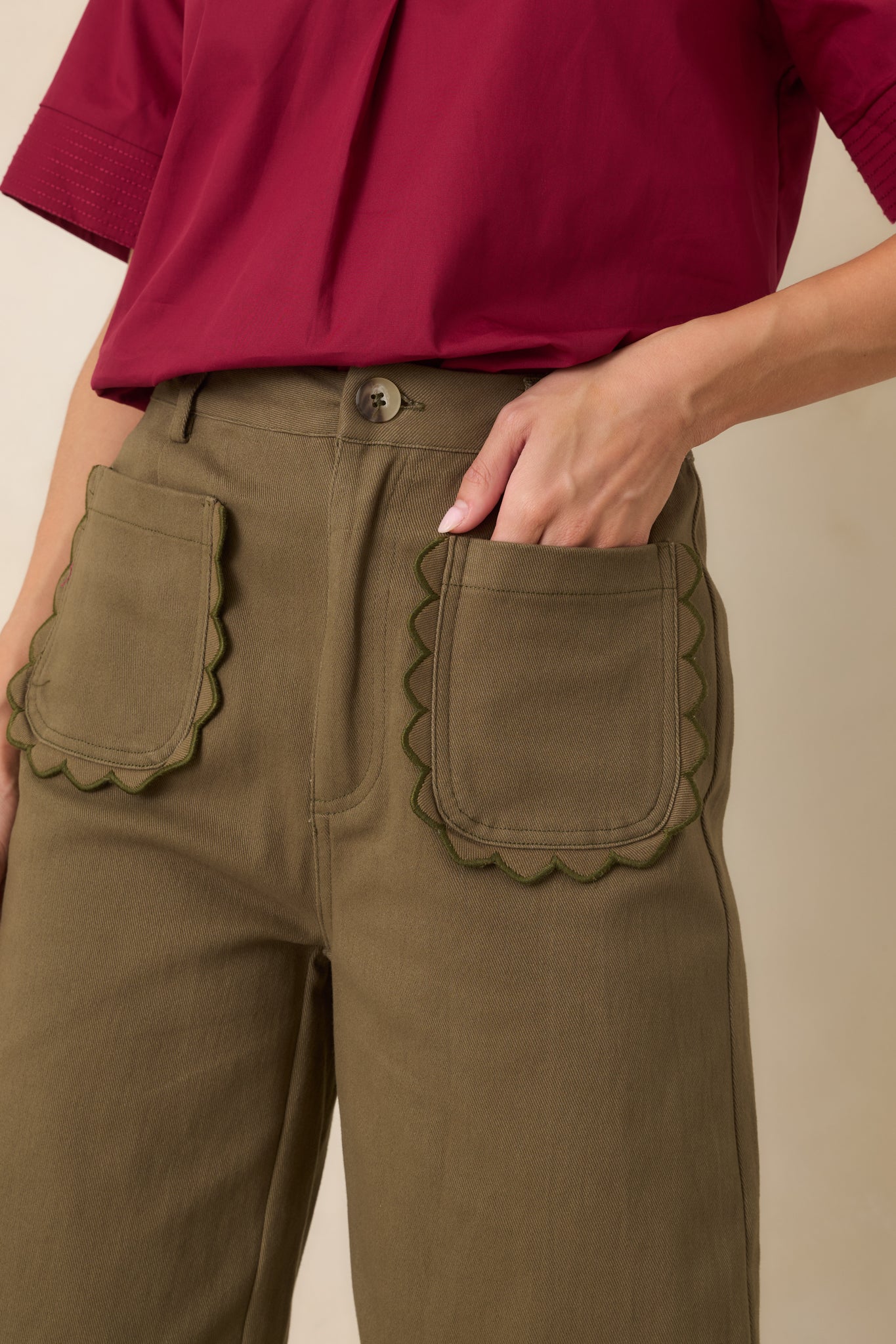Close-up of the woven cotton fabric displaying the scalloped pocket trim and rich olive green color.
