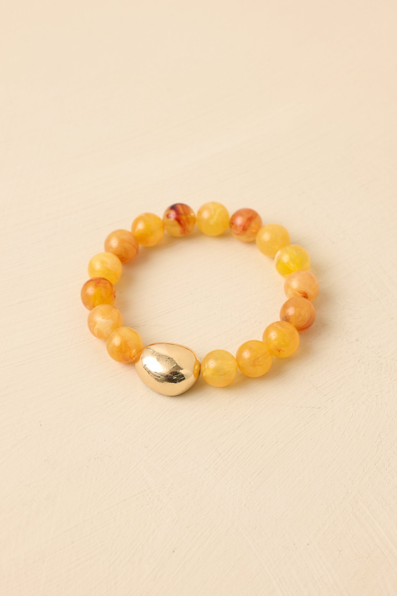 Yellow beaded bracelet displayed against a beige background featuring smooth beads and a gold-tone accent.