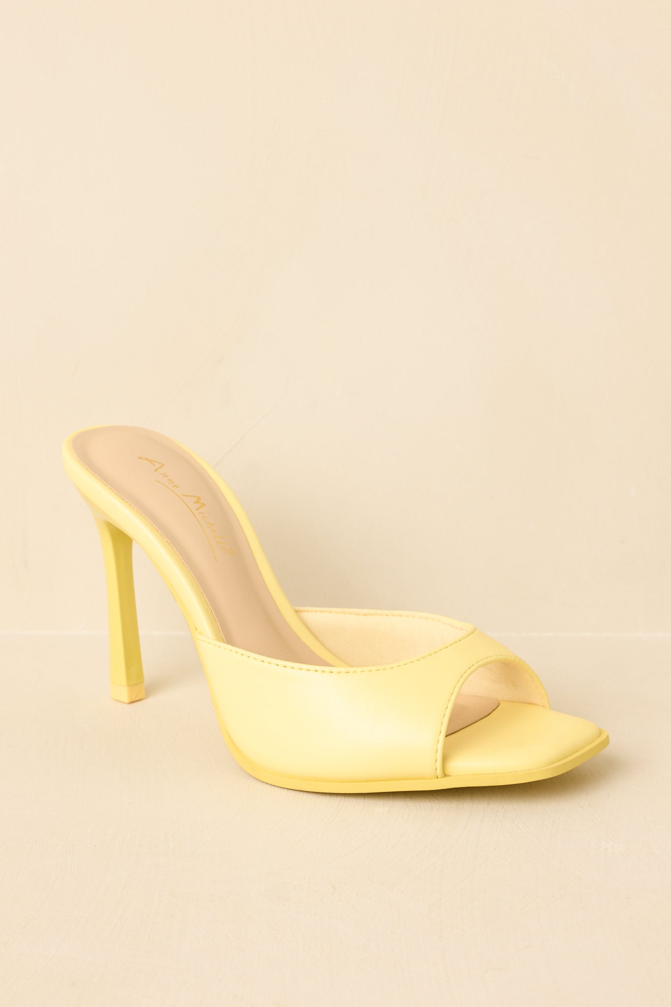 Three-quarter angle of yellow heeled mules on beige background emphasizing minimal design and vibrant color