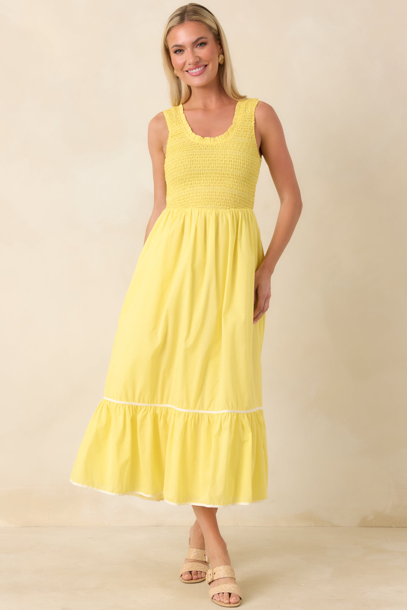 Yellow midi dress featuring a sleeveless scoop neckline, smocked bodice, and flowing tiered skirt with subtle ruffle hem.