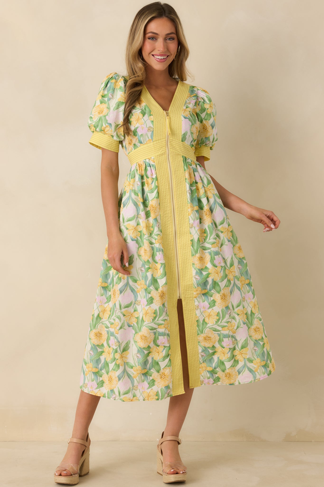 Yellow midi dress with a green and yellow floral print, V-neckline, short puff sleeves with cuffed hems, and a fitted waist flowing into a midi skirt with a subtle front slit.