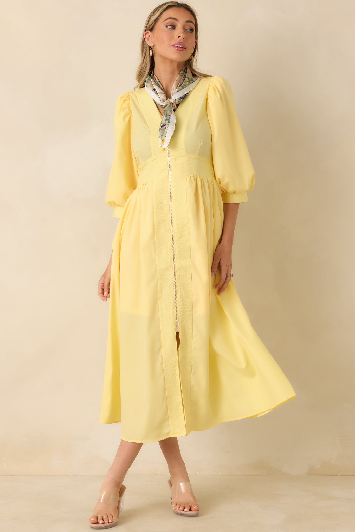 Yellow midi dress with a V-neckline, blouson sleeves, defined waistband, and a softly flared skirt with side pockets for movement.