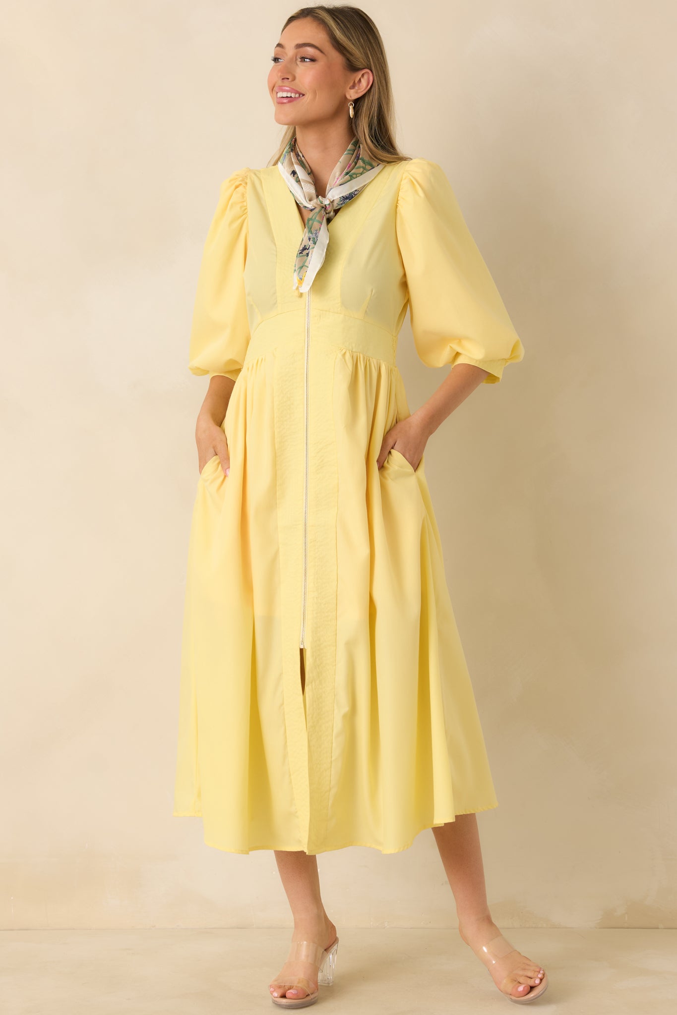 Yellow midi dress with a V-neckline, exposed front zipper, and blouson sleeves, featuring a defined waistband and flowing skirt.