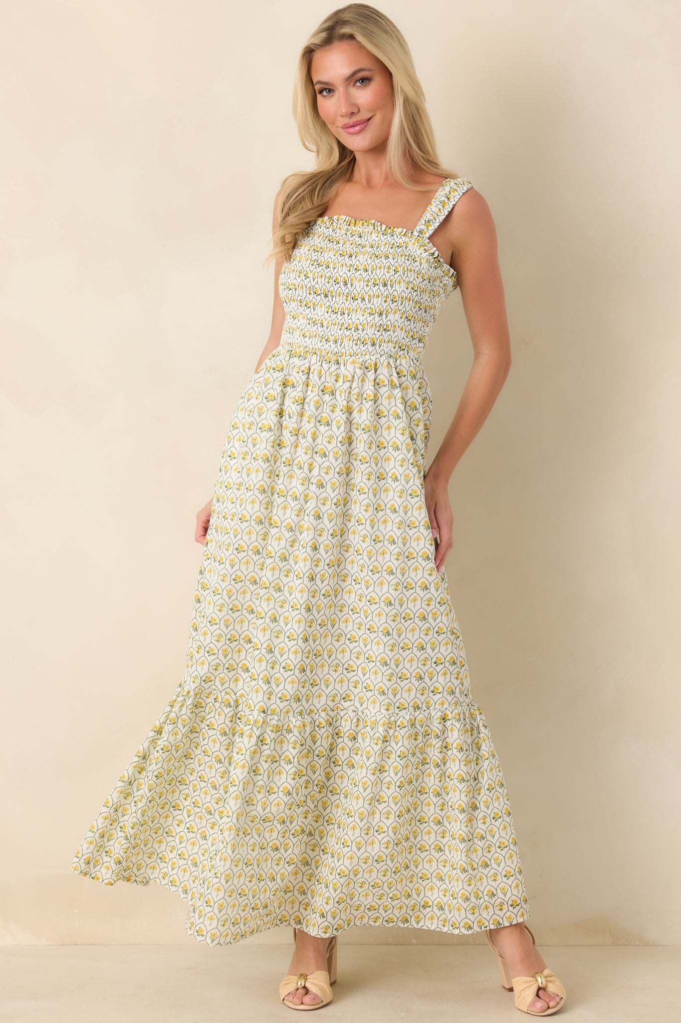 Yellow multicolor floral maxi dress with square neckline, wide straps, and fully smocked bodice flowing into a tiered skirt with side pockets.