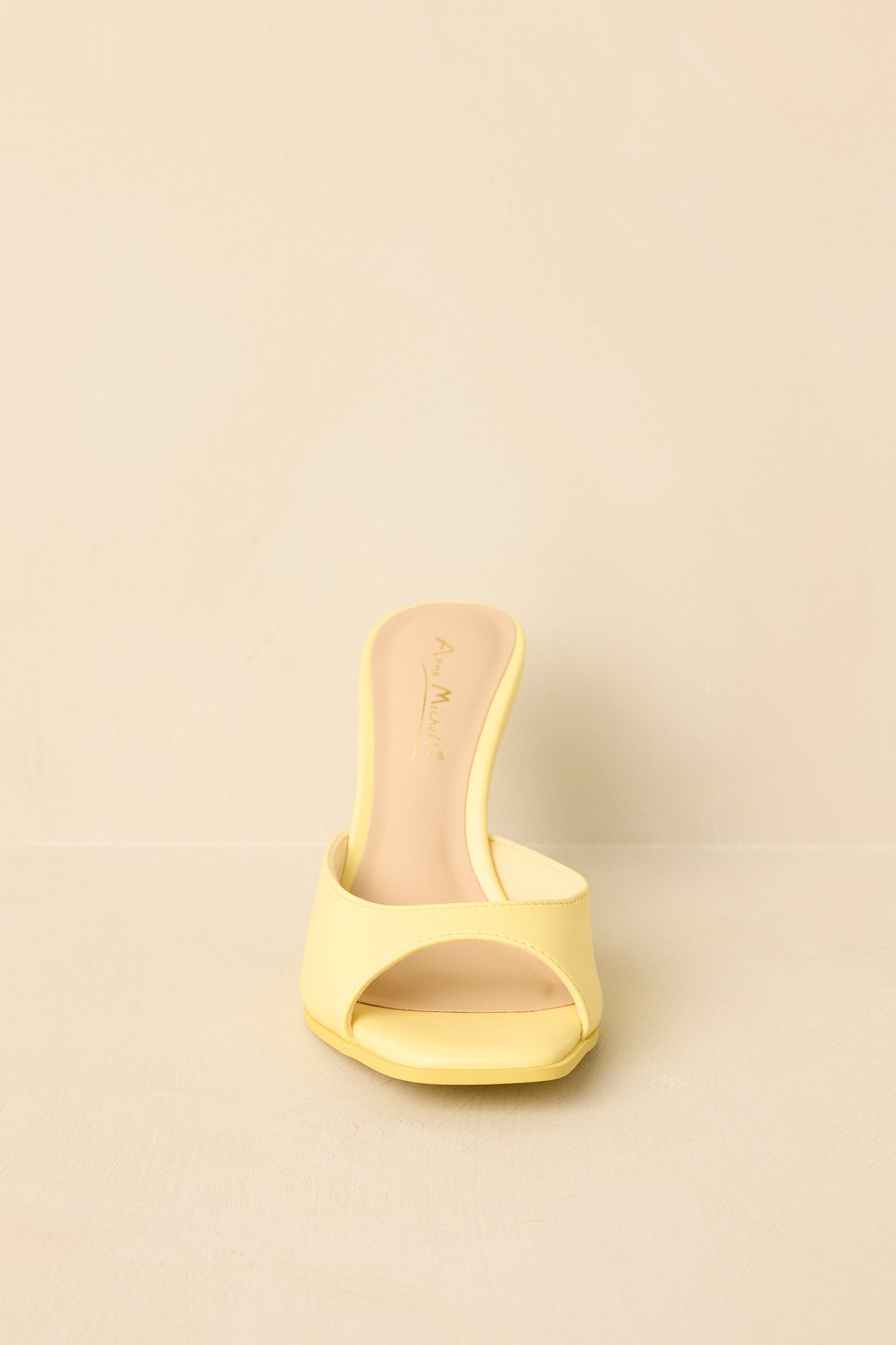 Yellow square toe heeled mule sandals displayed on a beige background, showcasing single strap and slim heel