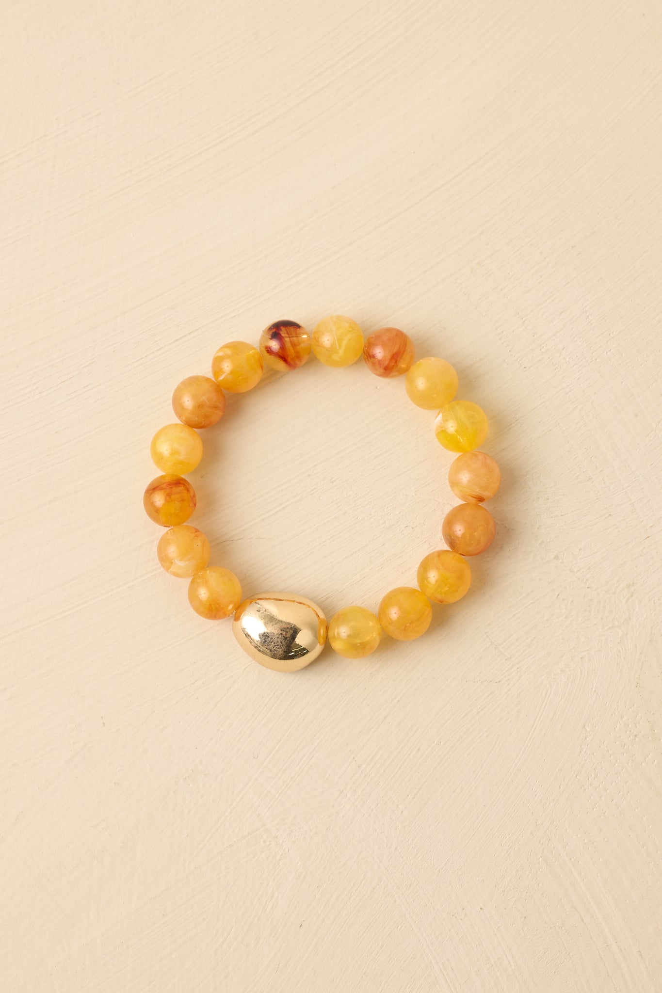 Stretch bracelet with polished yellow beads and a central gold-tone bead shown on beige.