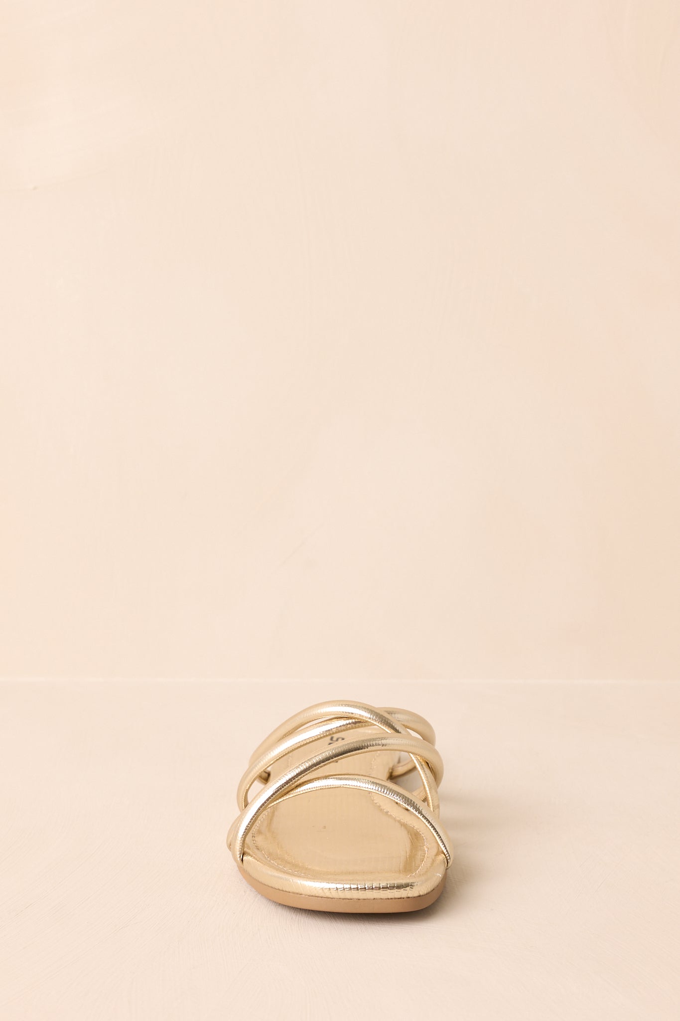 A zoomed-in frontal view of the gold sandals, displaying the metallic straps and open-toe shape.