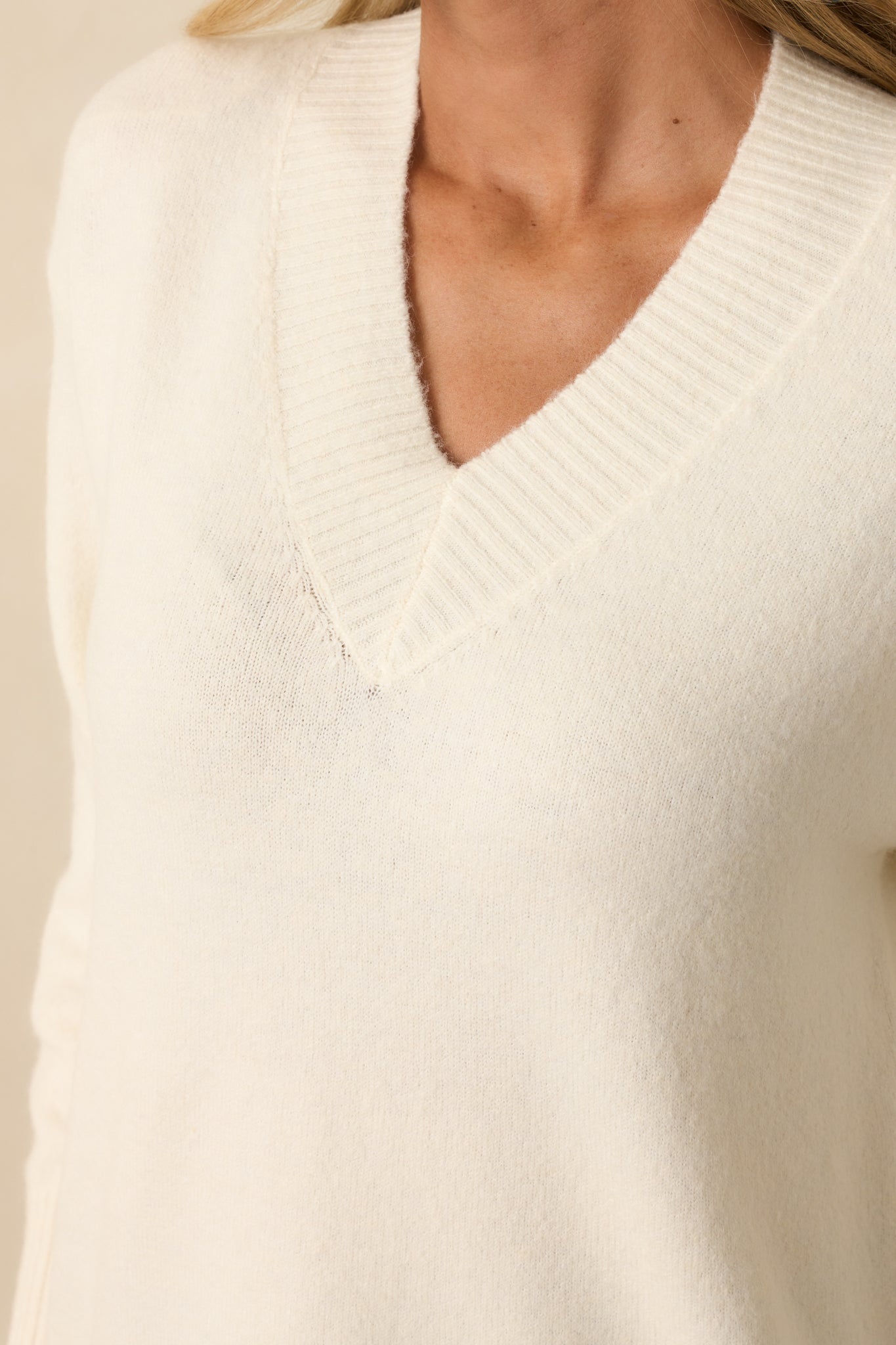 Zoomed-in view of the v-neckline, ribbed trim, and knit texture of the ivory sweater.