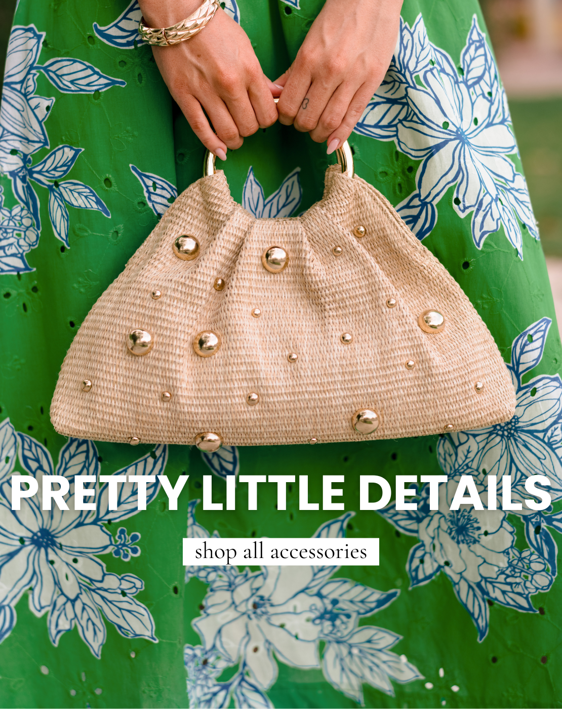 Close-up of a woven straw handbag with gold stud embellishments and metal handles, held by a model wearing a green floral dress. Text reads “Pretty Little Details – shop all accessories.