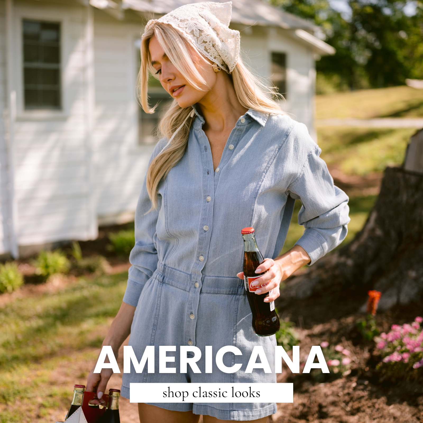 Model wearing a light wash denim romper with a lace headscarf, holding glass soda bottles outdoors in a sunlit countryside setting. Text reads “Americana – shop classic looks.”