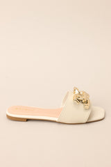 Side view of these ivory slip-on sandals that are adorned with a striking large gold buckle-like design, adding a touch of glamour to your ensemble.