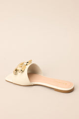 Angled back view of these ivory slip-on sandals that are adorned with a striking large gold buckle-like design, adding a touch of glamour to your ensemble.