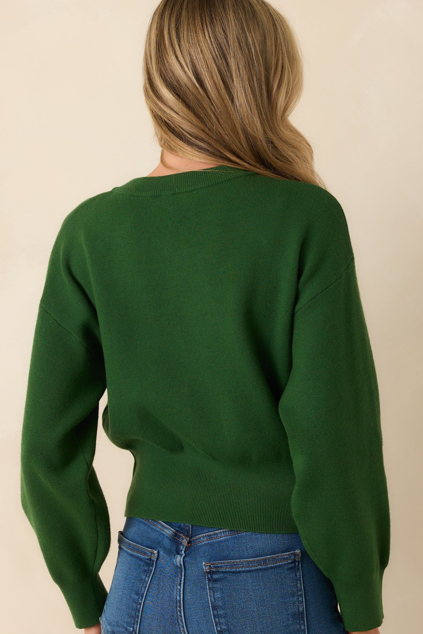 A view from behind of the hunter green cardigan, highlighting the smooth knit fabric, long sleeves, and ribbed waistband.