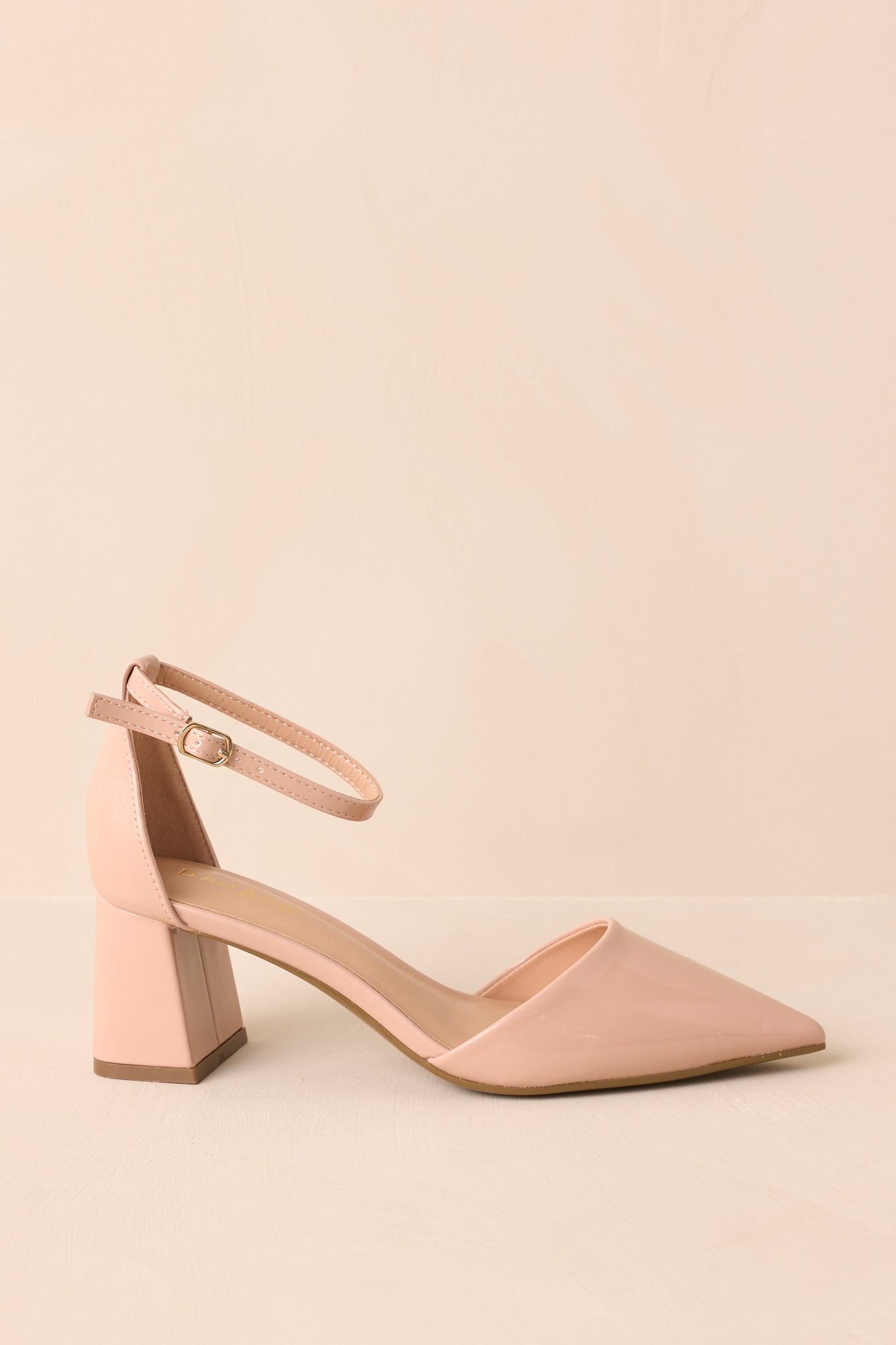 Full side view of the beige heels against a beige background, emphasizing the curved profile and block heel.