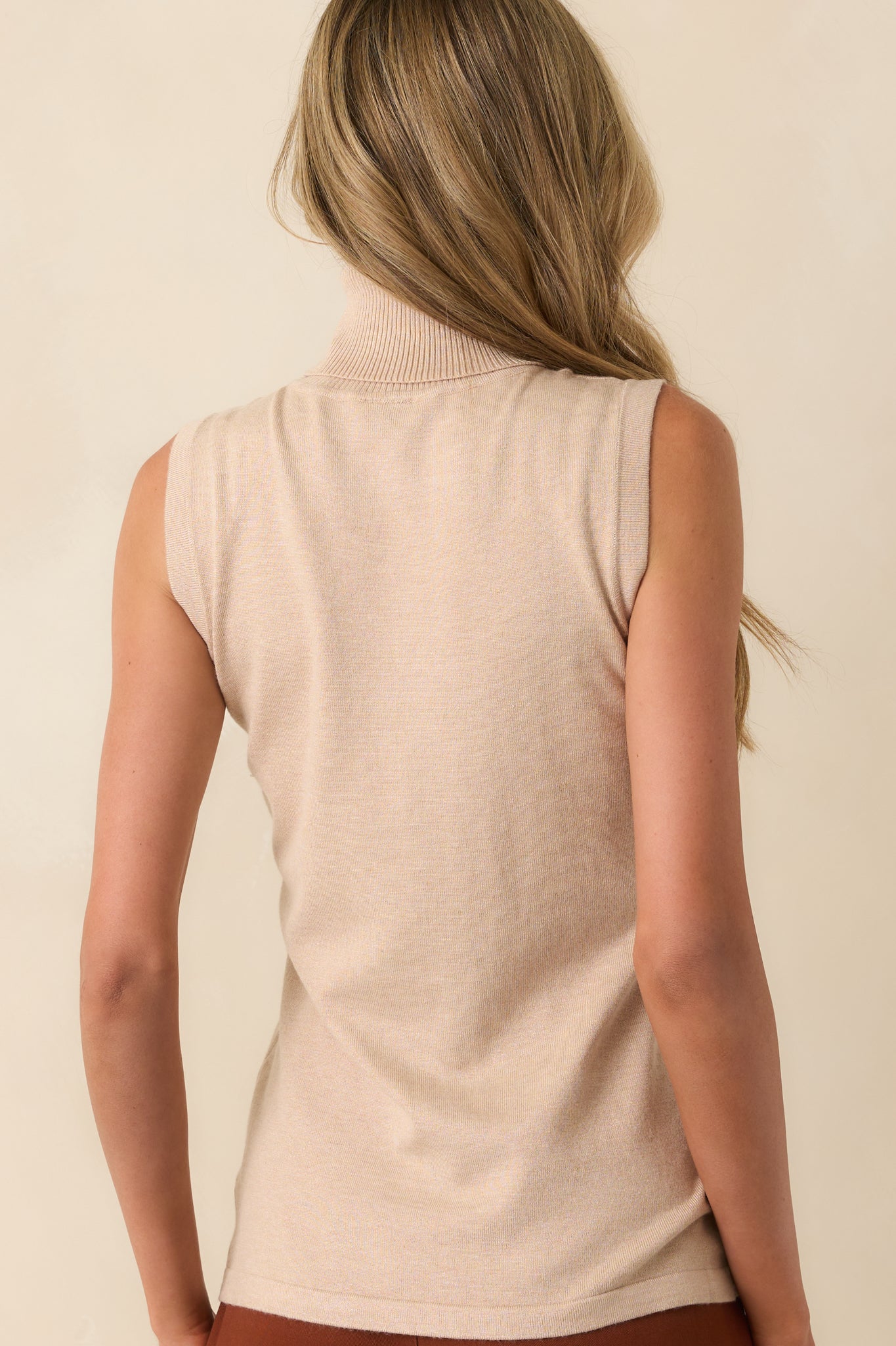 A view from behind showing the sleeveless shape, rolled turtleneck, and consistent ribbed texture across the back of the sweater.