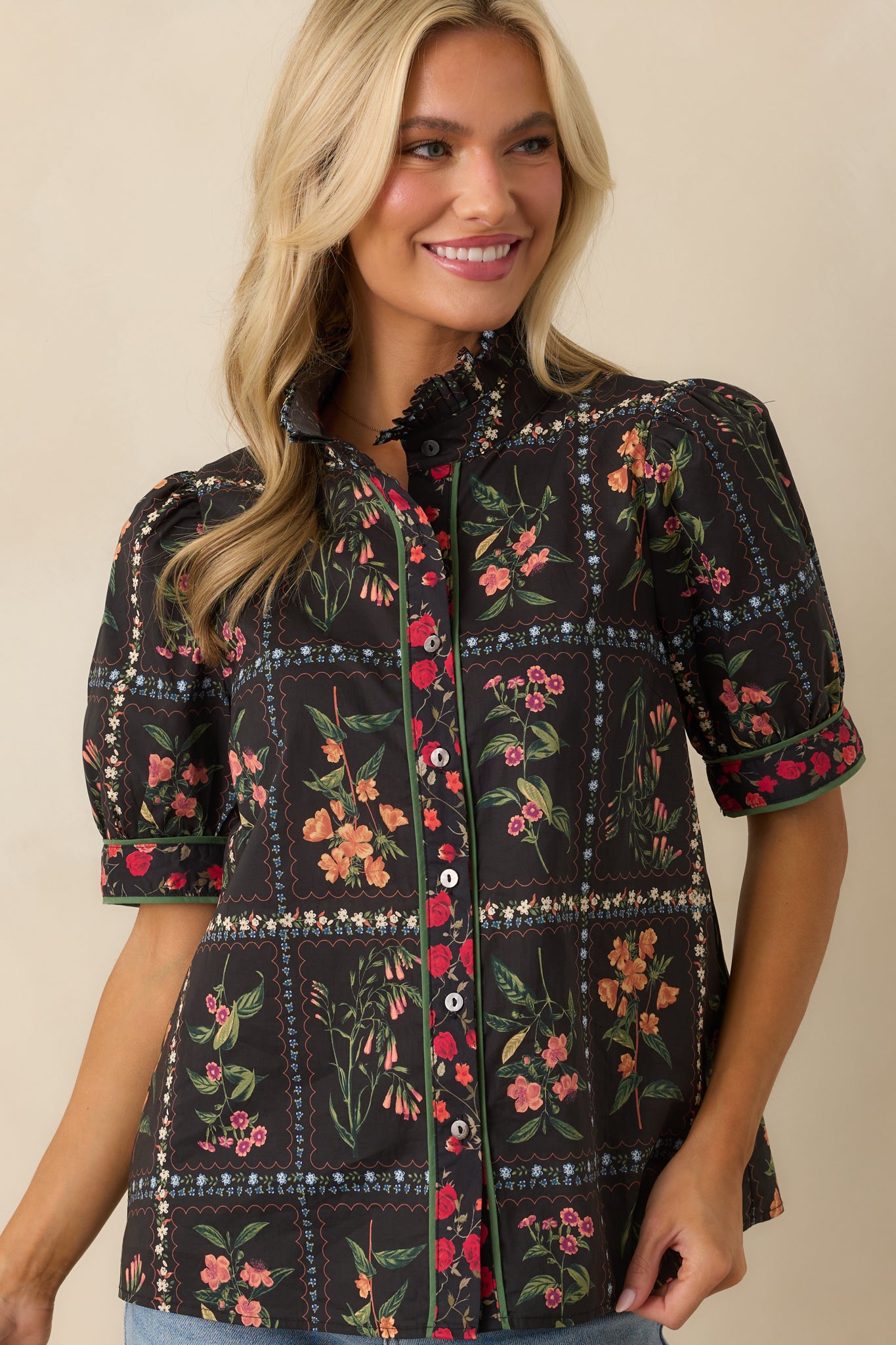 A close-up of the short puff sleeves with solid green trim on the black patchwork floral print top.