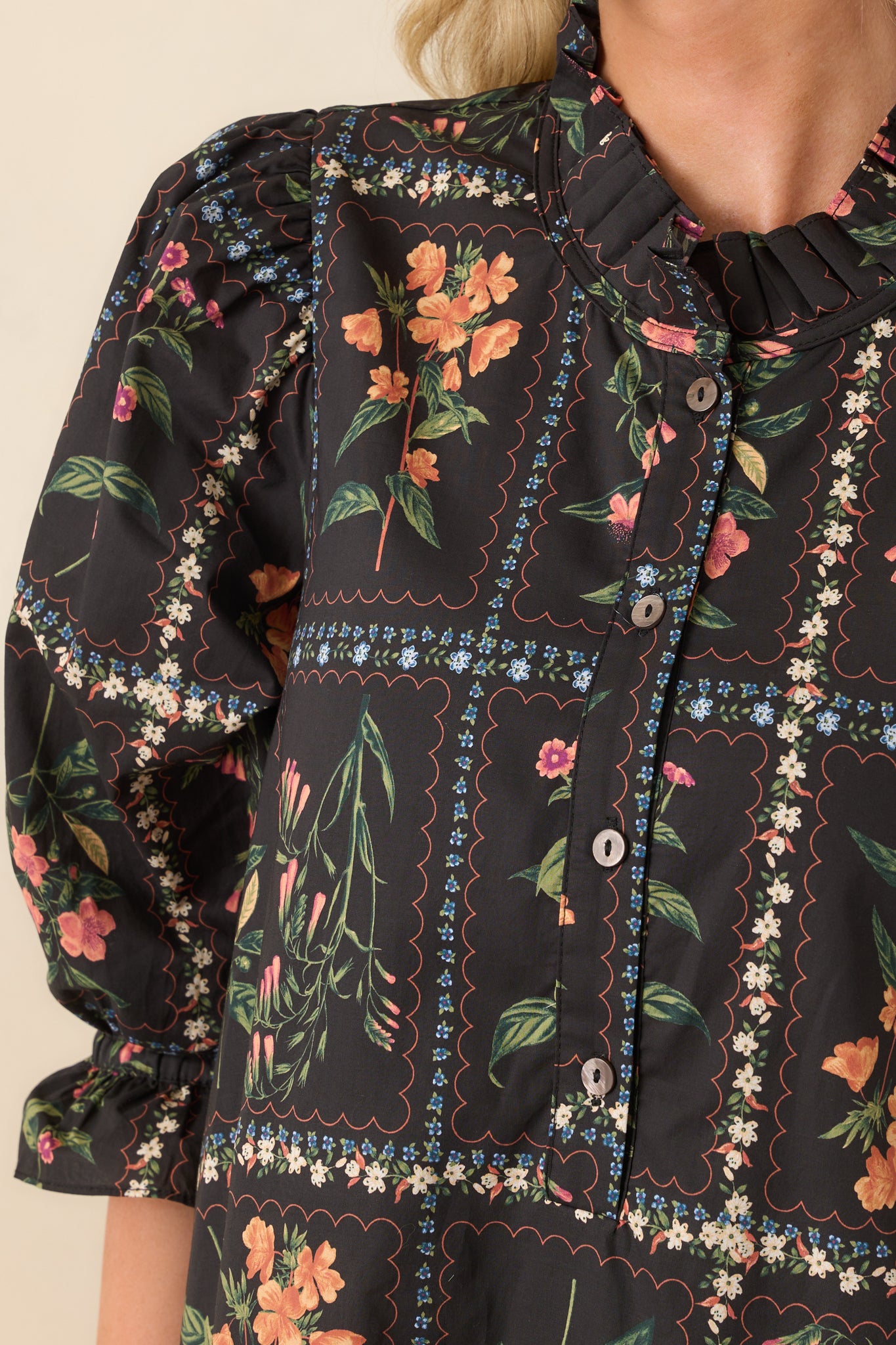 A close-up of the textured ruffle trim and floral detailing around the neckline and button placket.