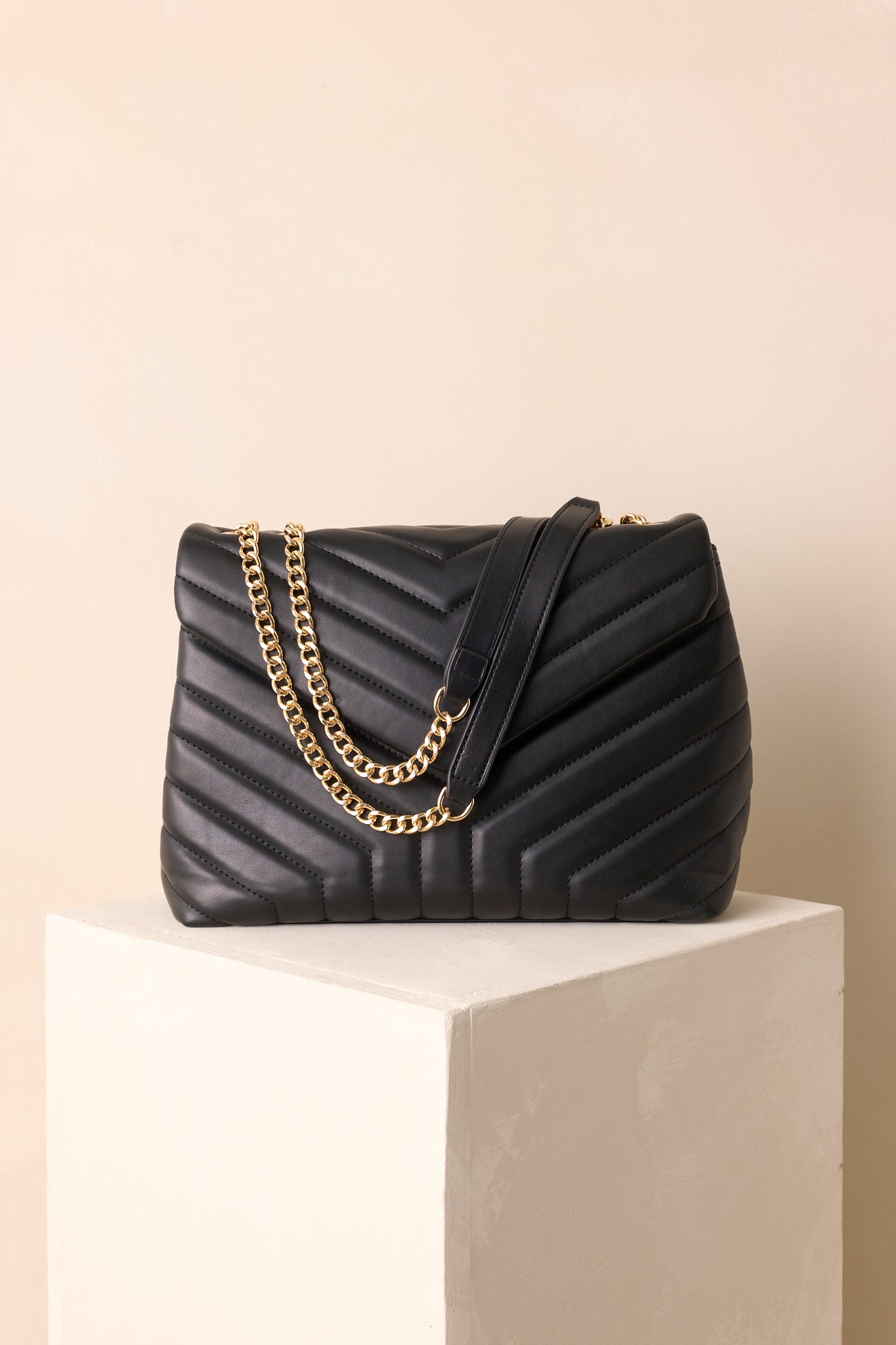 Black quilted rectangle handbag with gold chain handles and faux leather grips carried at the side.