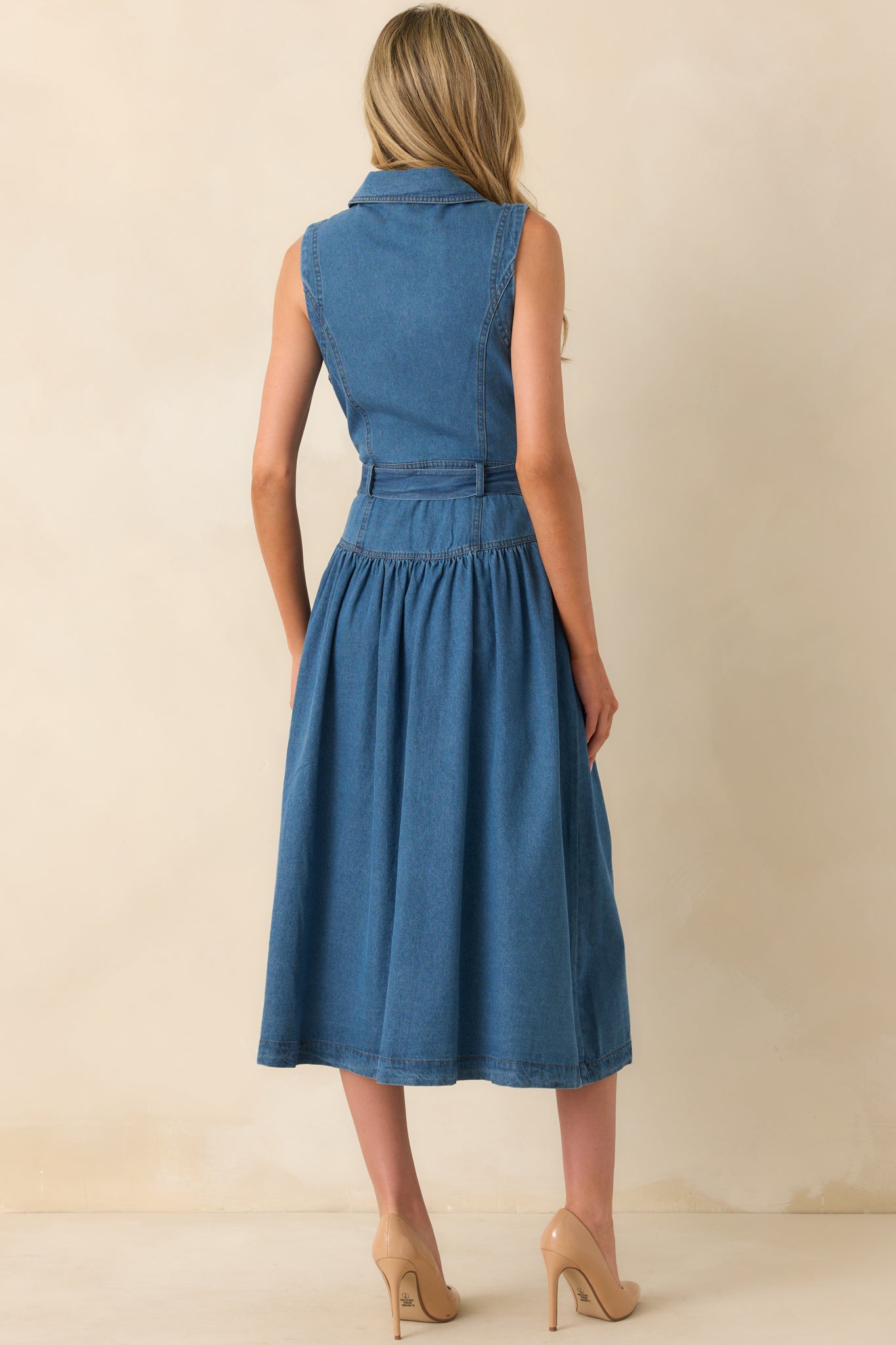 A back view of the blue denim midi dress with a sleeveless cut and drop waist seam.