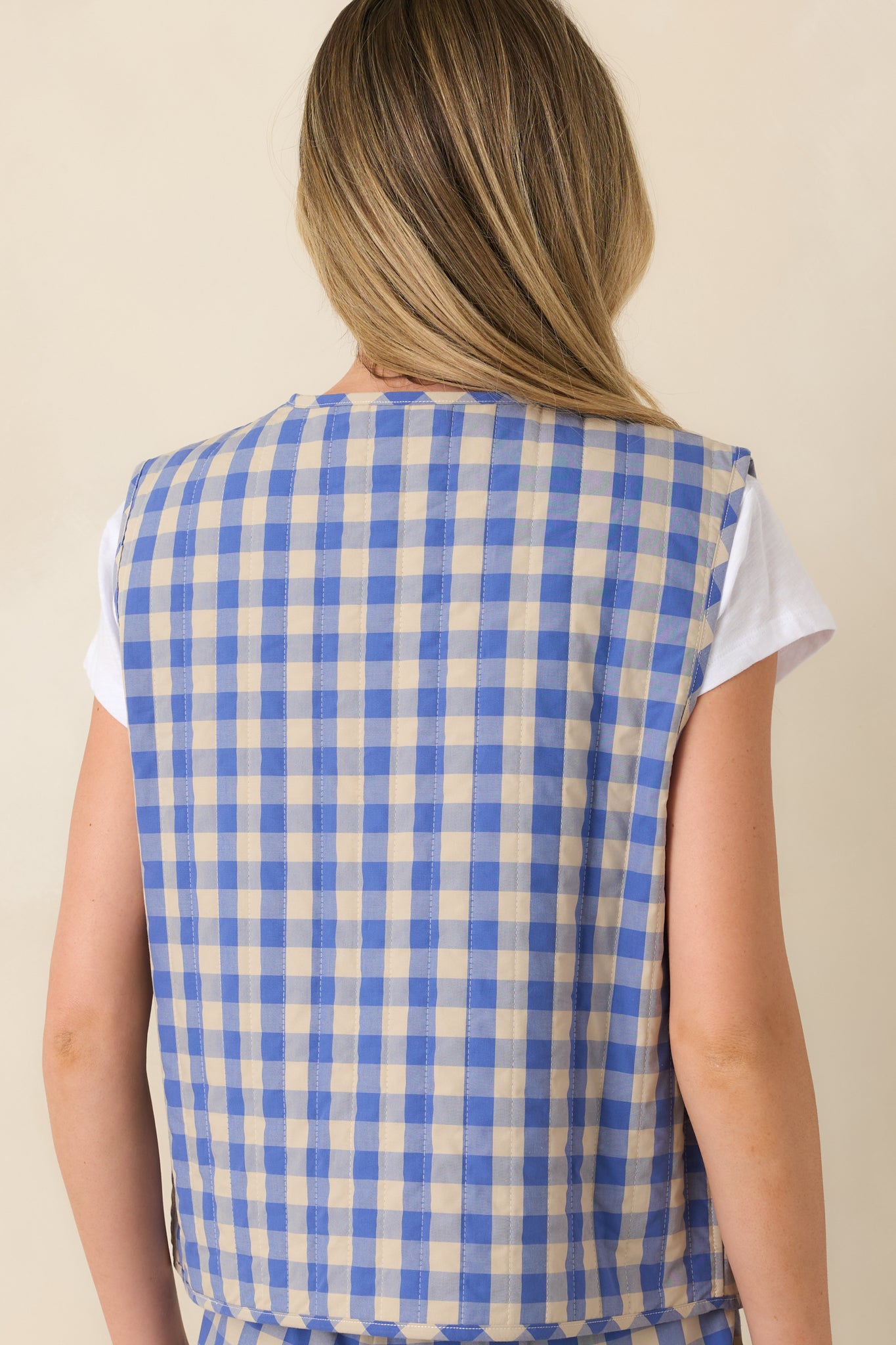 Back view of a blue gingham quilted vest featuring an allover gingham print and quilted stitching.