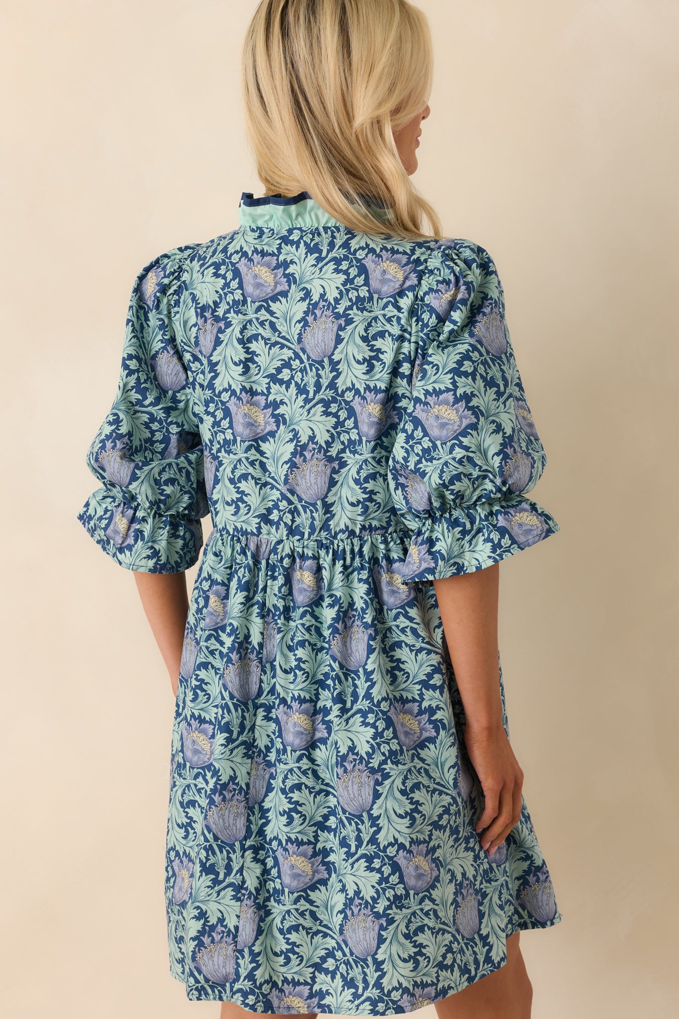 A view from behind showing the navy mini dress with half puff sleeves and smooth back fabric.