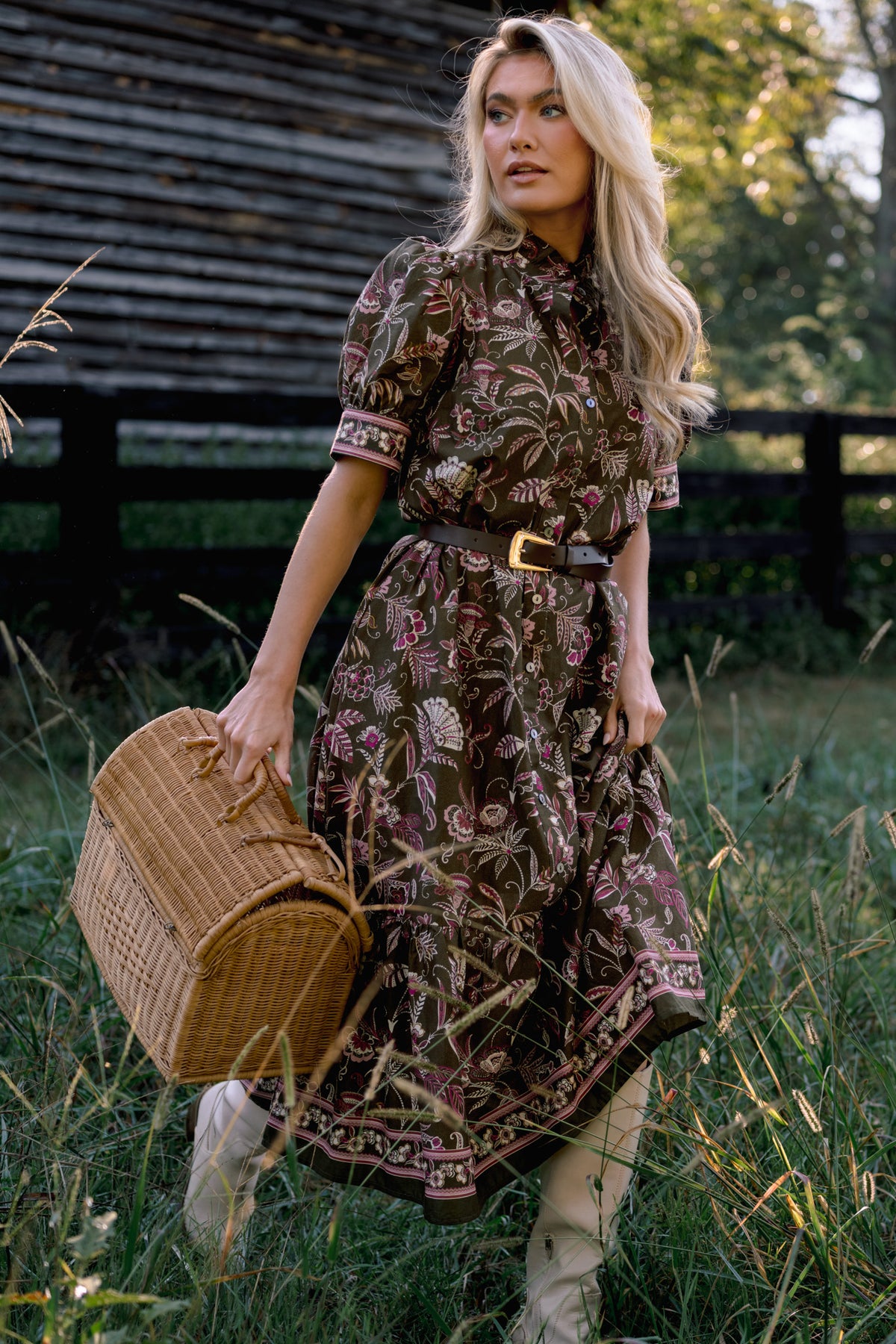 Model wearing a brown floral midi shirt dress with short sleeves, a collared neckline, and a dark belt, carrying a wicker basket outdoors.