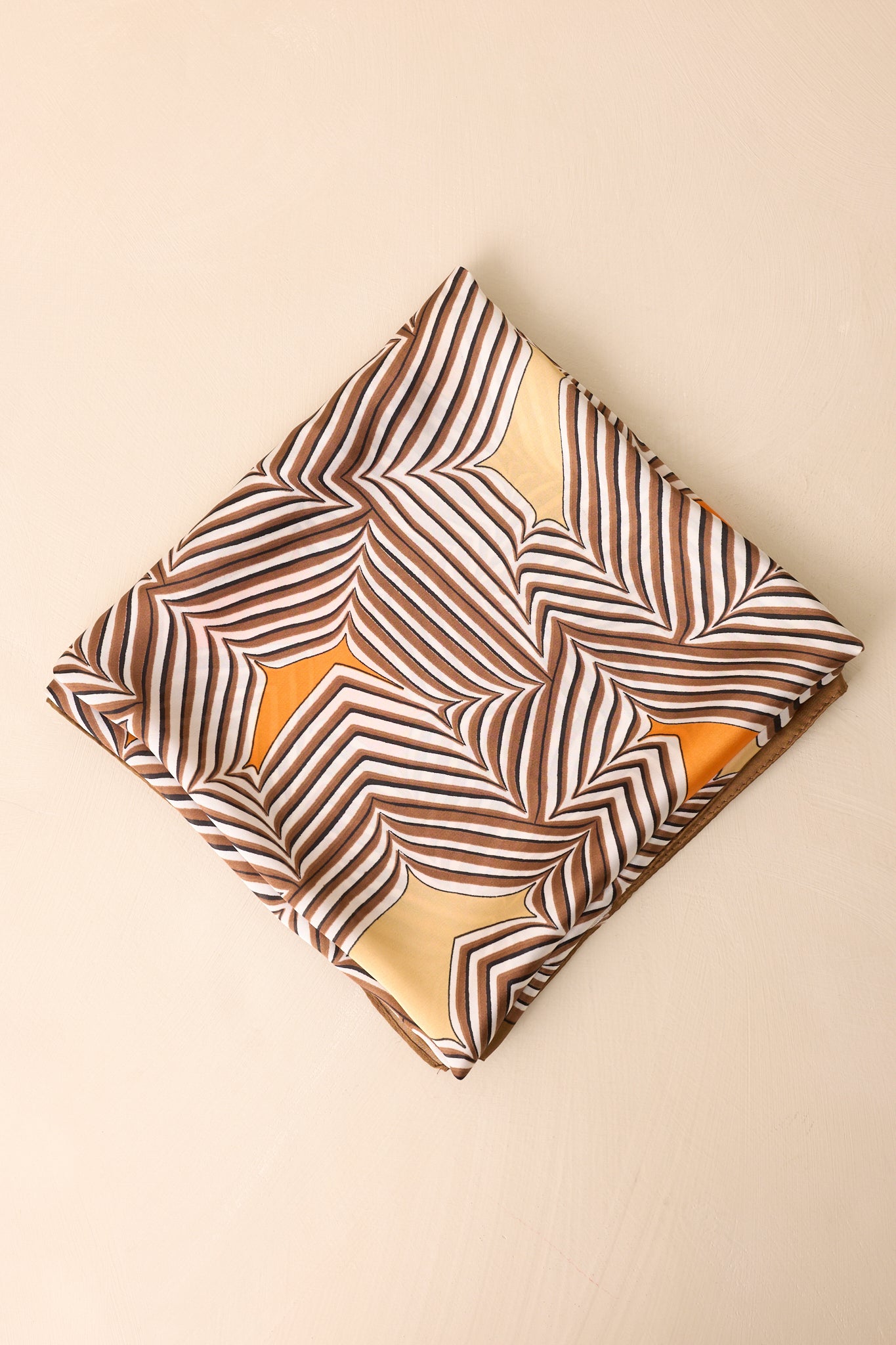 Brown scarf folded into a small square, displaying portions of the geometric stripe print and vibrant orange and golden yellow color details.