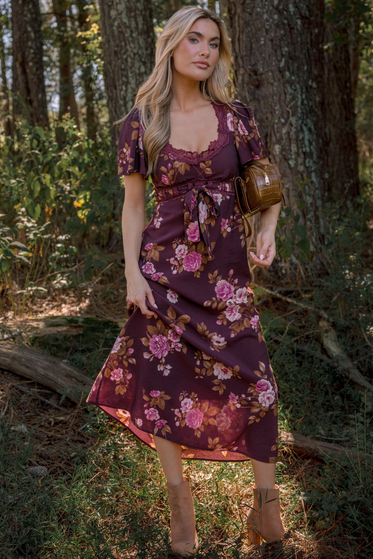 Model wearing a burgundy floral midi dress with short puff sleeves, a lace-trim scoop neckline, and a tie waist, standing outdoors.