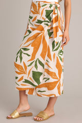 Side view of this tropical print midi skirt that features a high waisted design, an elastic waist insert, self-tie wrap features, an orange & green tropical print, and a lightweight fabric.