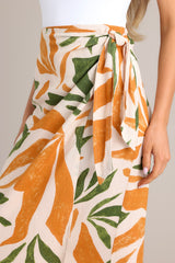 Close up view of this tropical print midi skirt that features a high waisted design, an elastic waist insert, self-tie wrap features, an orange & green tropical print, and a lightweight fabric.