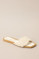 Front angled view of  these ivory flats that feature a square toe, a slip-on design, and a strap across the top of the foot with a knitted texture. 