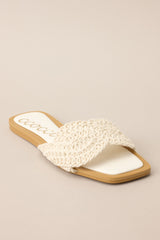 Angled view of  these ivory flats that feature a square toe, a slip-on design, and a strap across the top of the foot with a knitted texture. 