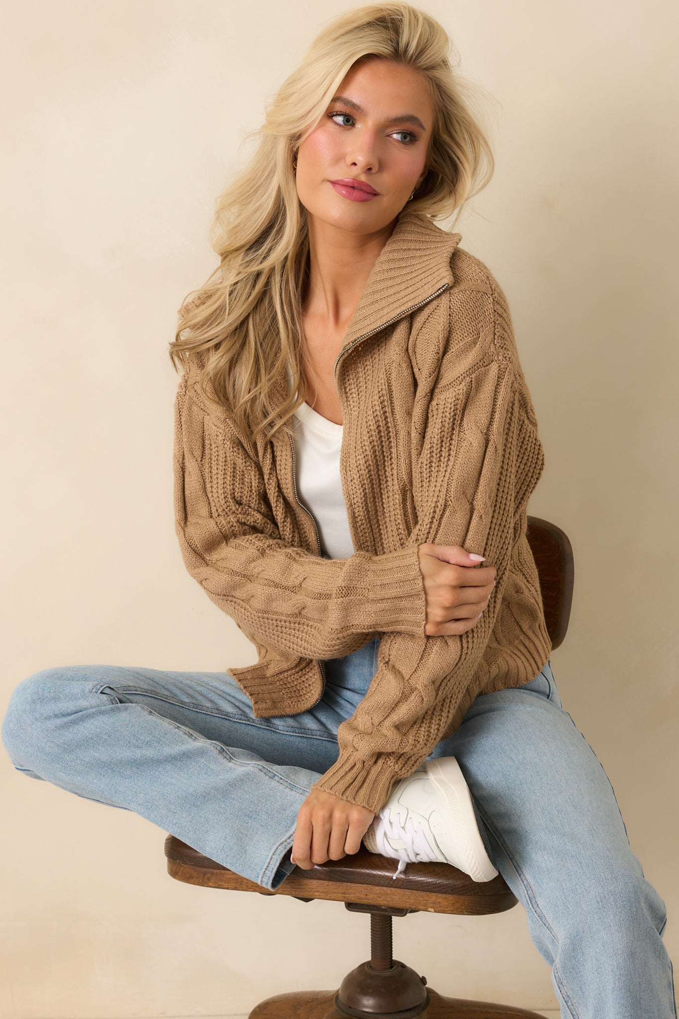 Camel brown cable knit sweater jacket with a zip front and ribbed trim worn in a classic casual style.