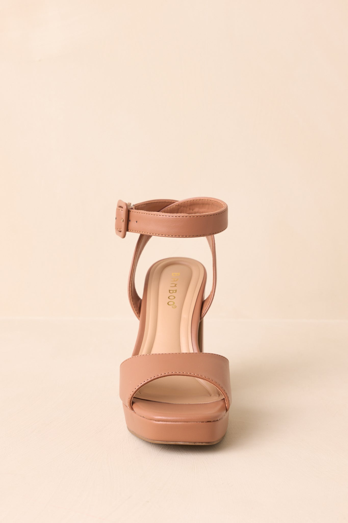 Front view of the brown heels on beige background highlighting the square toe and ankle strap.