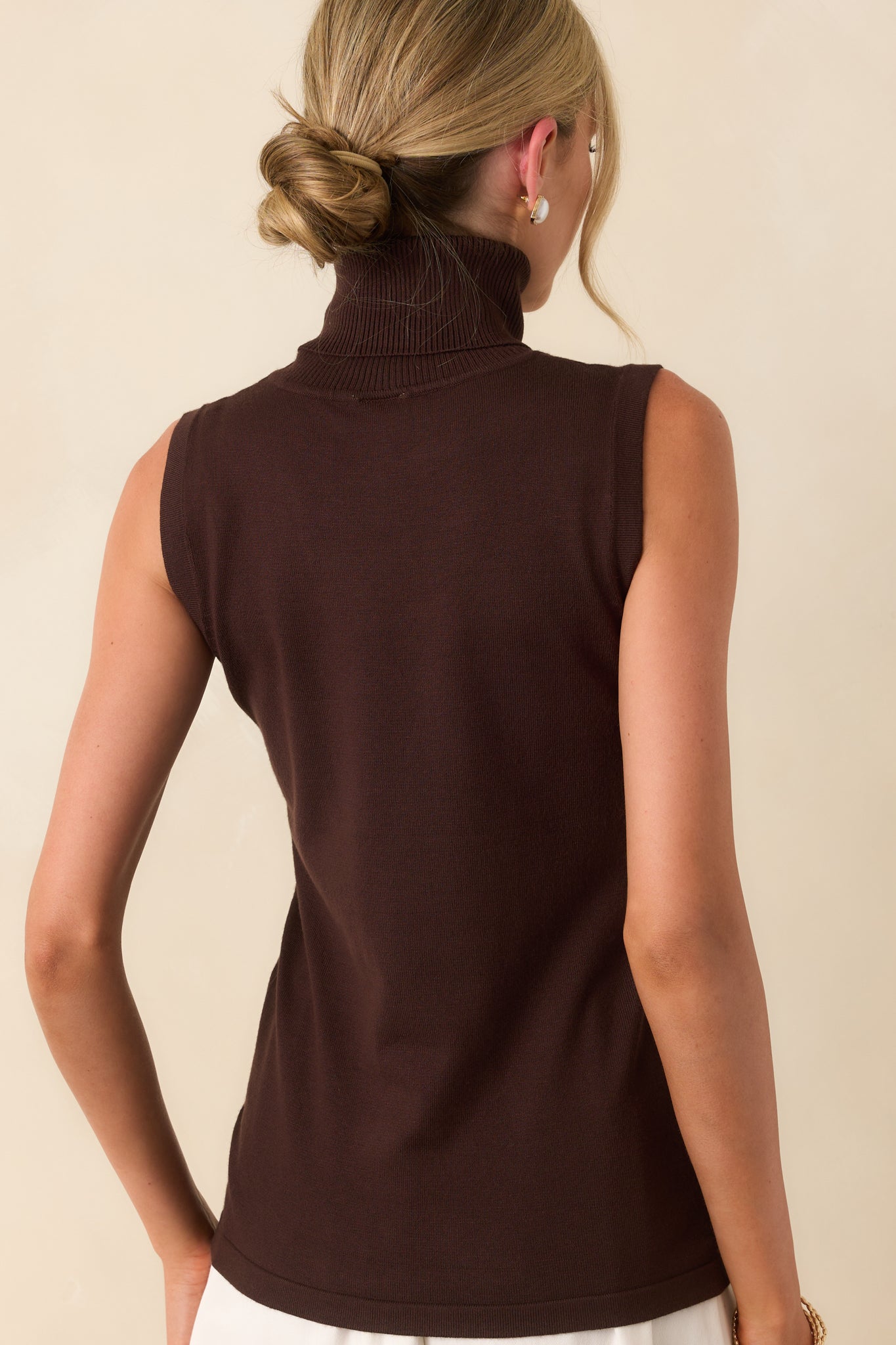A view from behind showing the sleeveless shape, rolled turtleneck, and consistent ribbed texture across the back of the sweater.