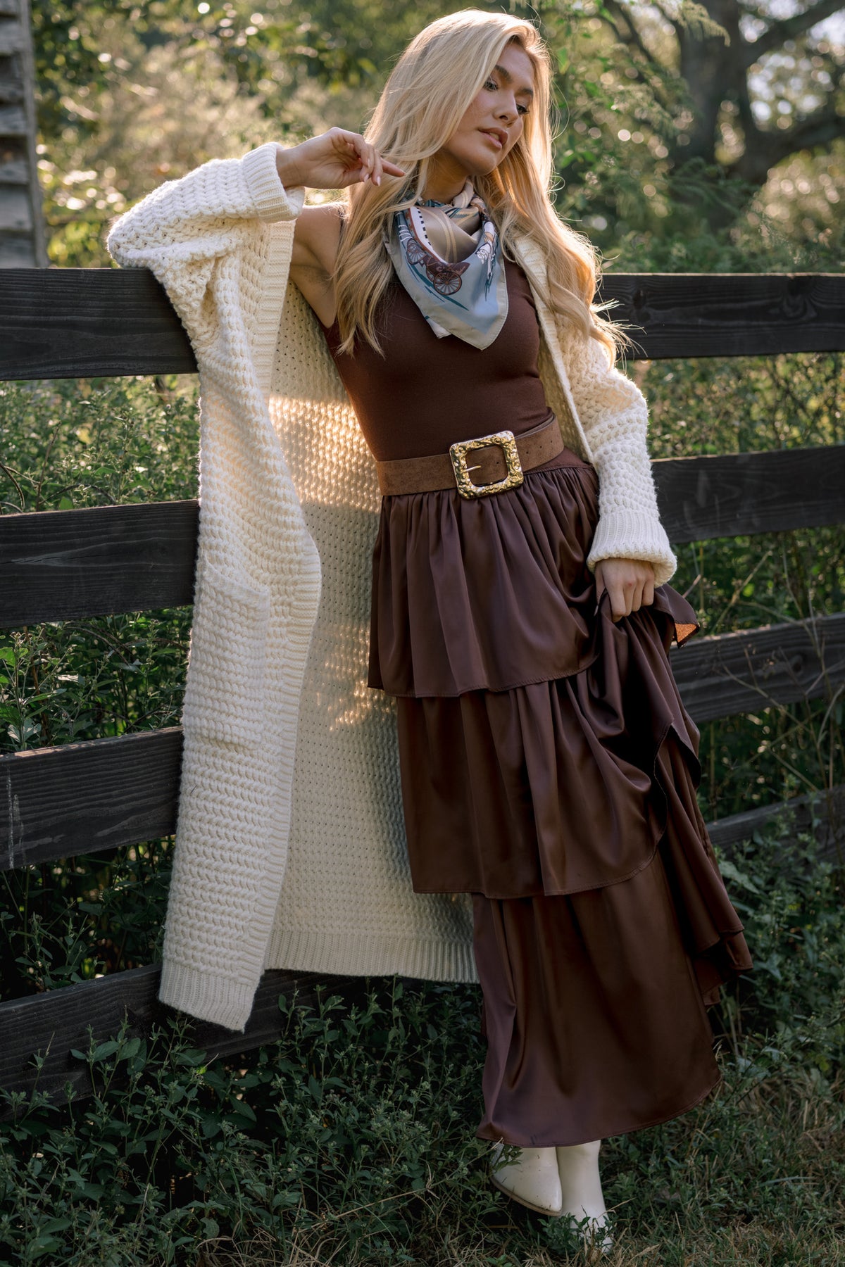Model wearing a chocolate brown tiered maxi dress with a wide belt, styled with a cream knit cardigan and ankle boots.
