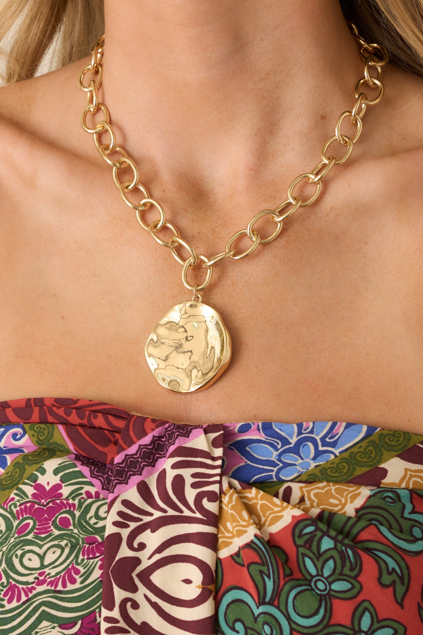 Cropped view of chunky gold chain necklace with abstract organic-shaped pendant and hammered texture.